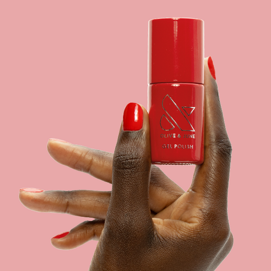 CV - Gel bottle held by hand with matching bright cherry red gel polish for a vibrant, long-lasting mani by Olive and June
