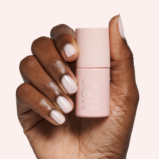 Hand holding Dream Job - Gel polish bottle with neutral milky sheer pink gel manicure on pale background
