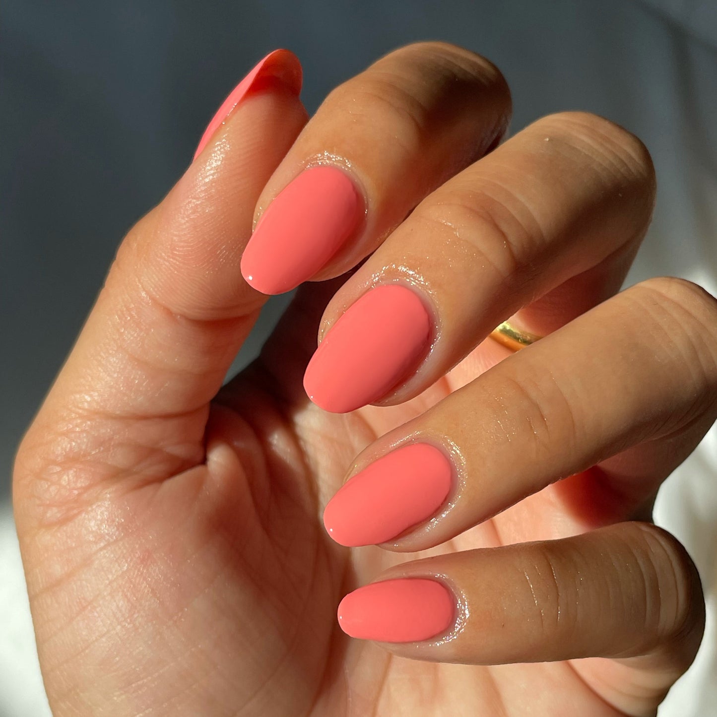 Hand with nails painted in glossy Stinson Sunset gel polish by Olive and June showing a bright coral manicure