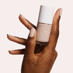 Hand holding a bottle of CDJ nail polish with nails coated in a creamy neutral gel polish finish