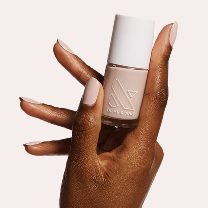 Hand holding a bottle of CDJ nail polish with nails coated in a creamy neutral gel polish finish