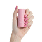 Hand with polished nails holding a pink Olive and June Nail Strengthener bottle on a light skin tone