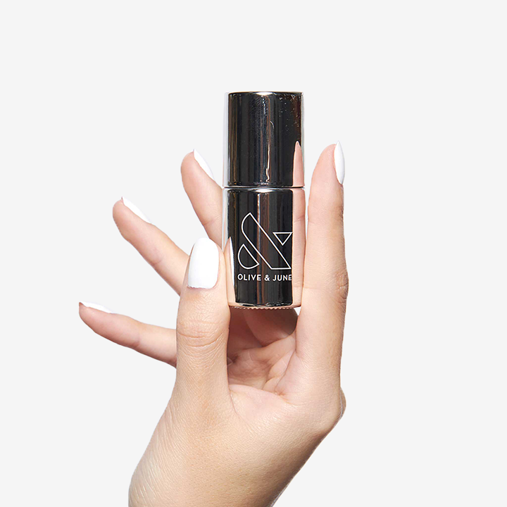 Hand holding Olive and June Long Lasting Top Coat with white polished nails for manicures and at-home manis