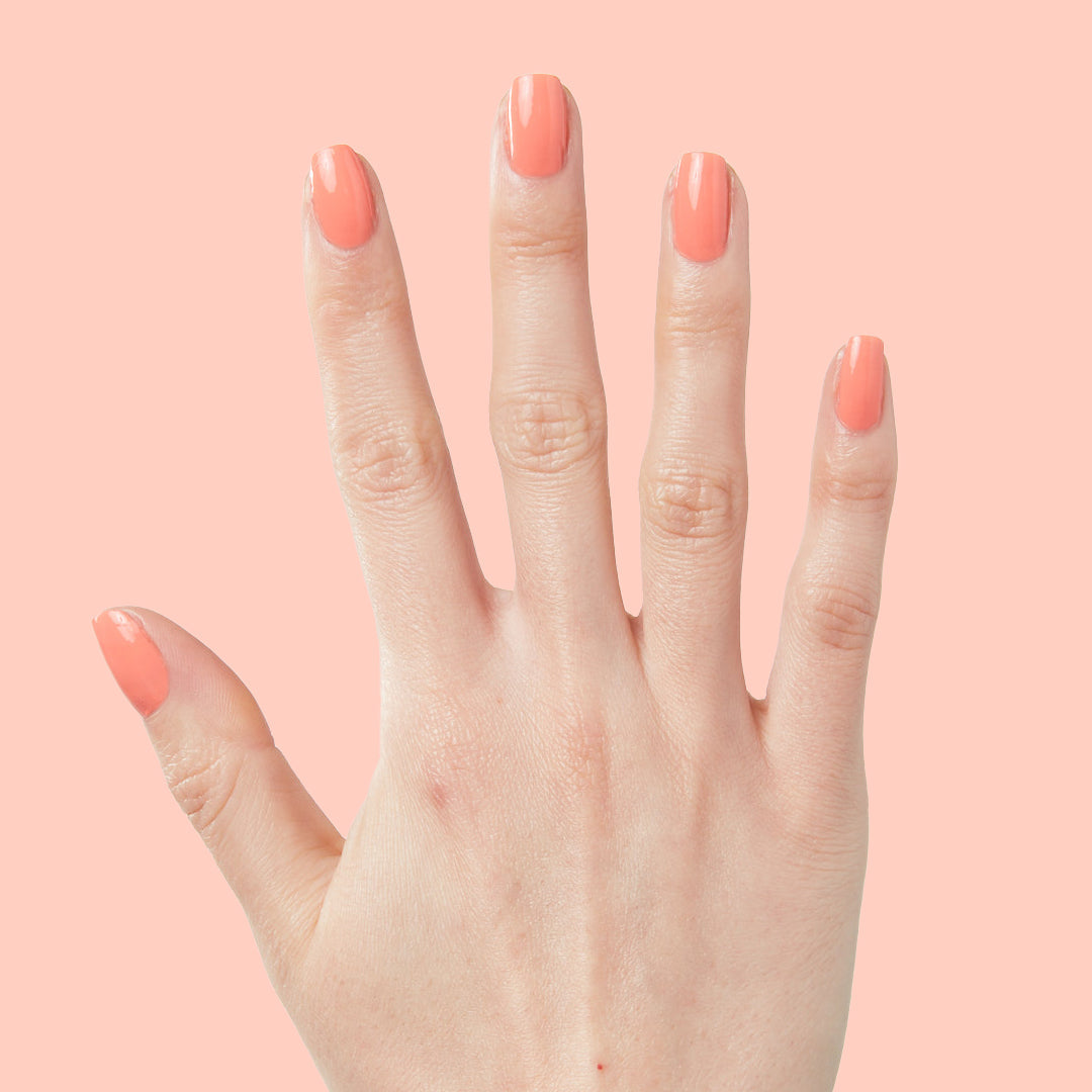 Hand with nails painted in bright cantaloupe orange Counselor In Training gel polish on pale peach background