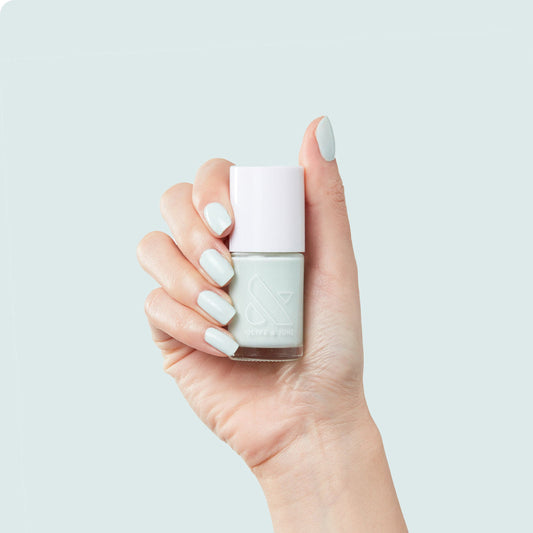 Hand holding Sleeping Bag polish bottle with pastel mint green nails against light blue background