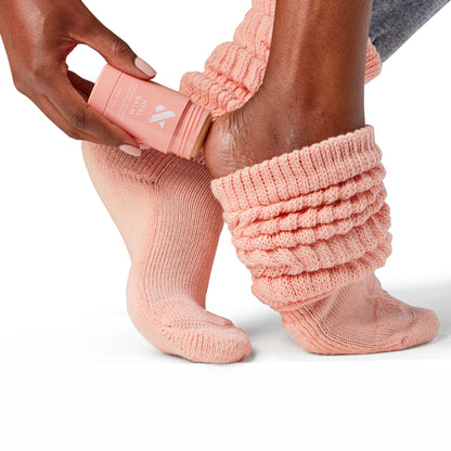 Person wearing peach knit socks applying Heel Balm stick to heel for dry and cracked skin care treatment