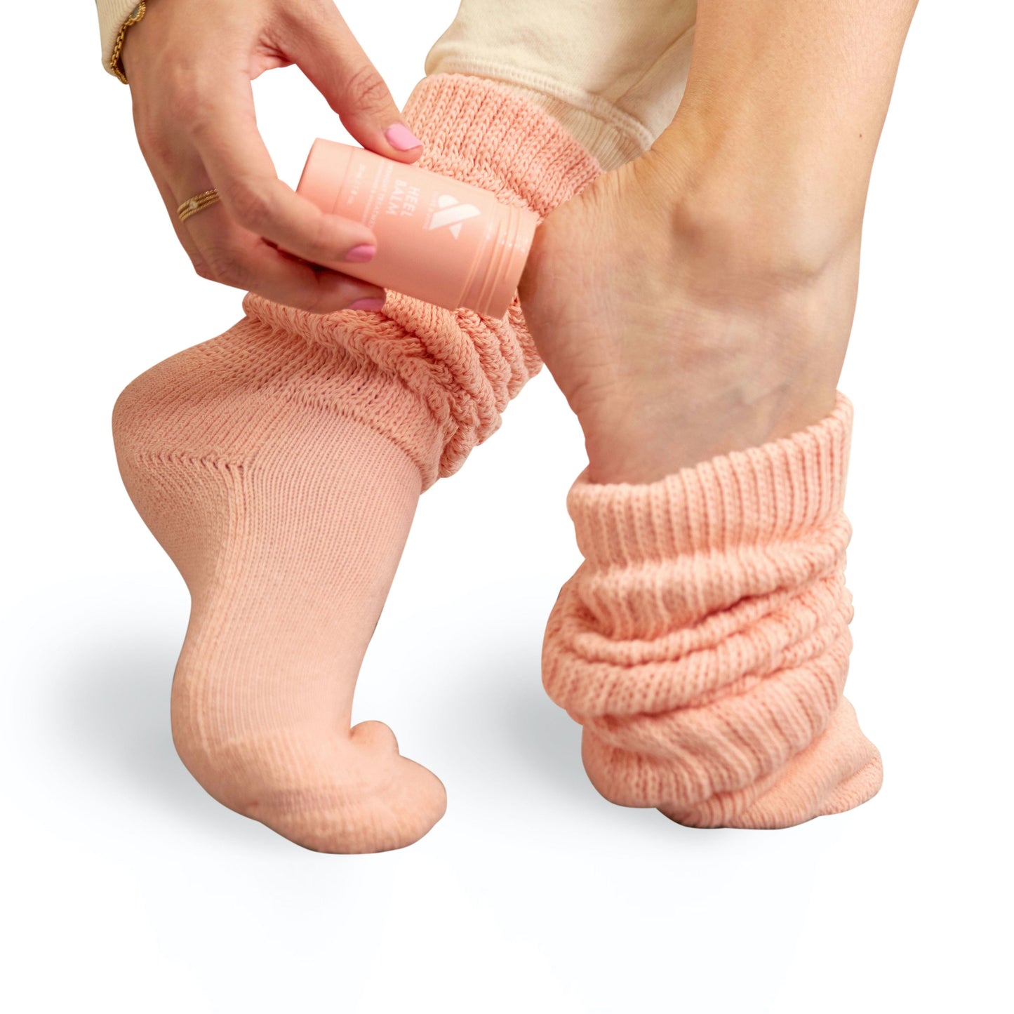 Person applying Overnight Heel Repair Set balm to heel while wearing slouchy peach knit socks on white background