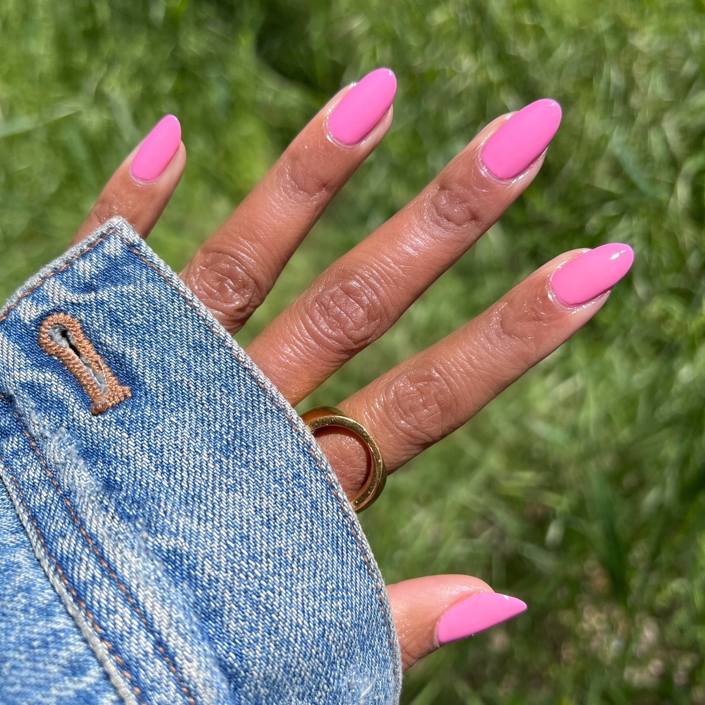 Hand outdoors with nails painted in bright pink Taffy quick dry gel polish wearing a gold ring and denim jacket sleeve