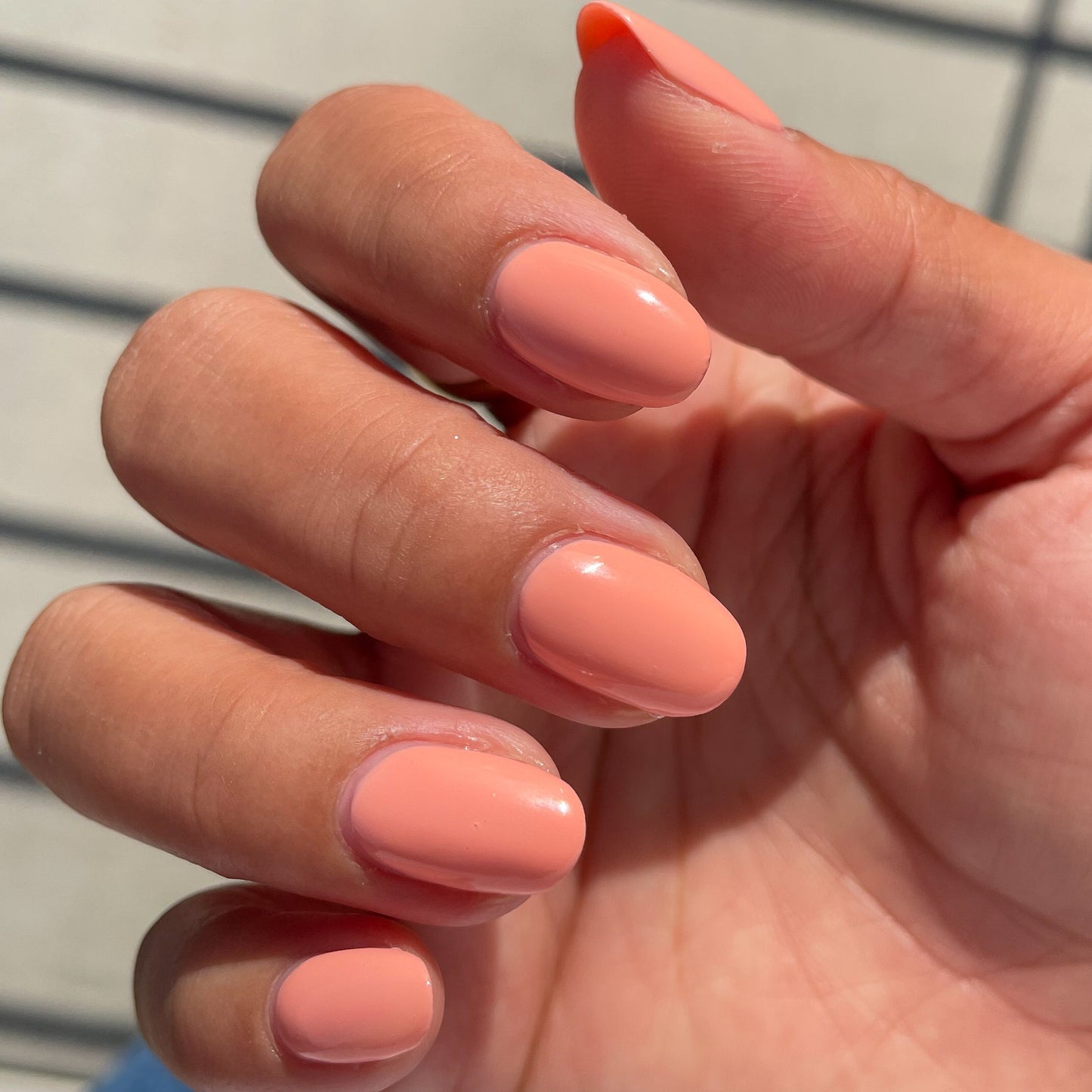 Hand with glossy nails painted in soft coral Wild & Free gel polish for a smooth at-home manicure look
