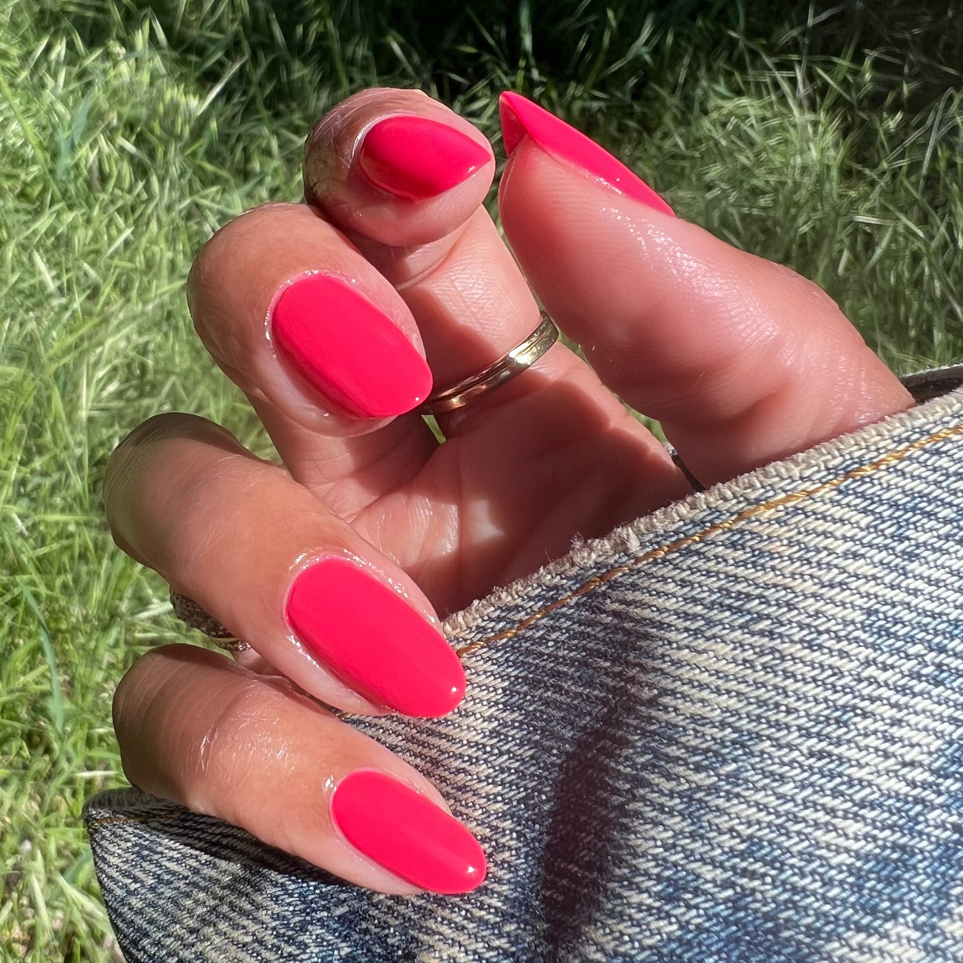 Hand with Pomodoro nail polish in bright pinky-tomato red on natural nails held over denim fabric outdoors