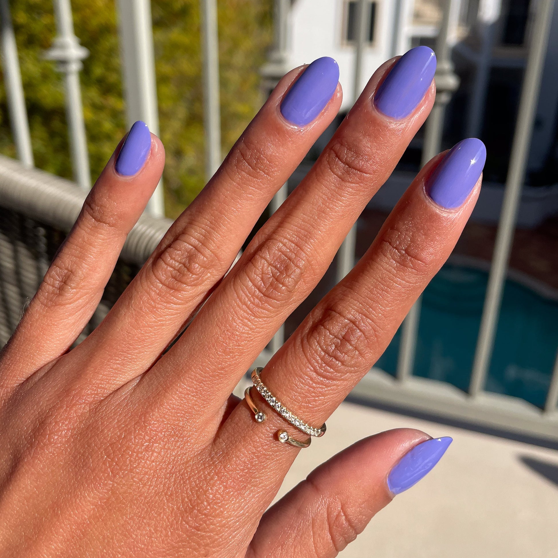 Hand with Royal quick dry gel polish in glossy regal purple on natural nails by a bright outdoor pool setting