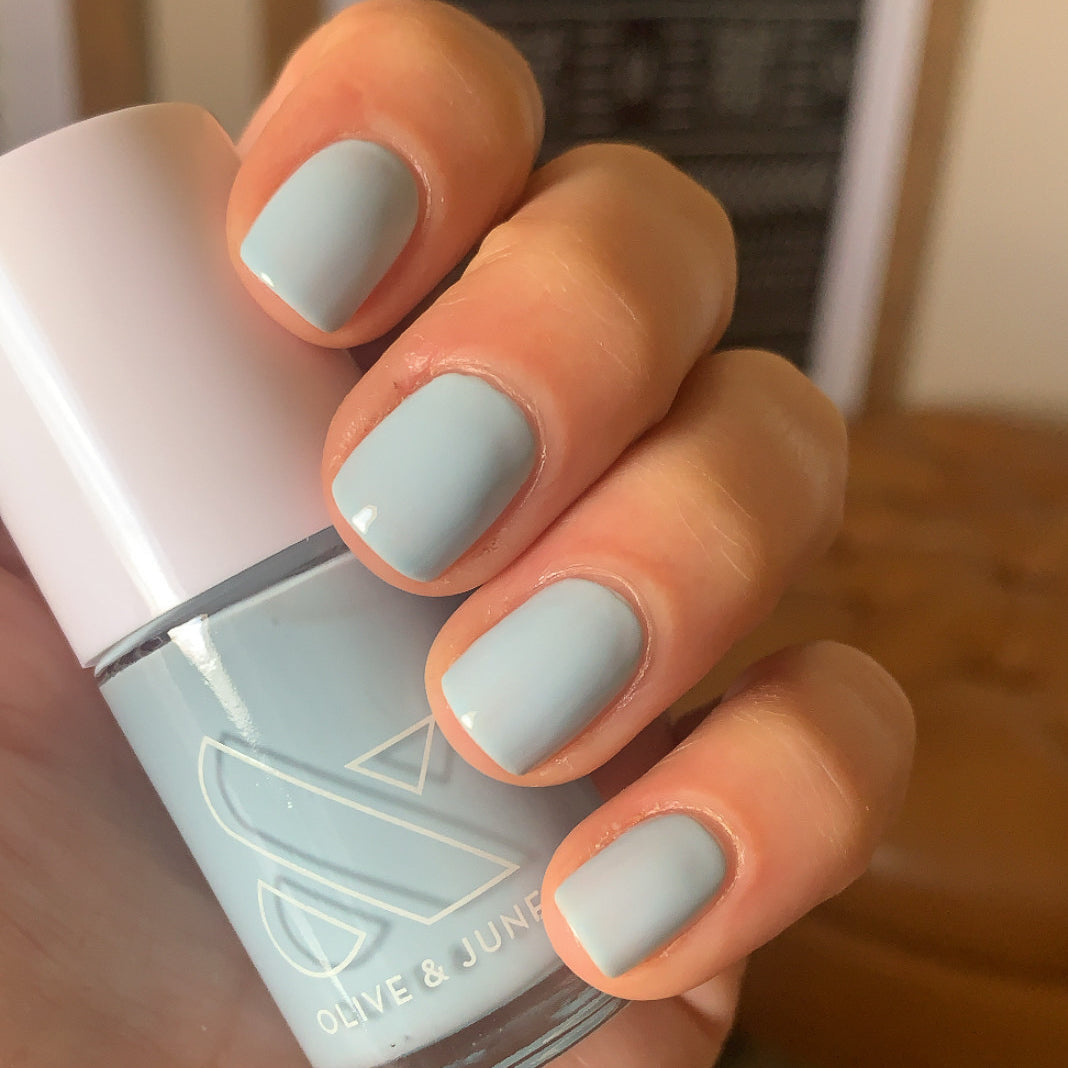 Hand holding Olive & June Honest & True nail polish with nails painted in a soft, calming blue gel polish mani