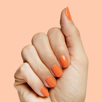 Hand with short nails painted bright tangerine using Bounce Back nail polish for a fresh at-home mani
