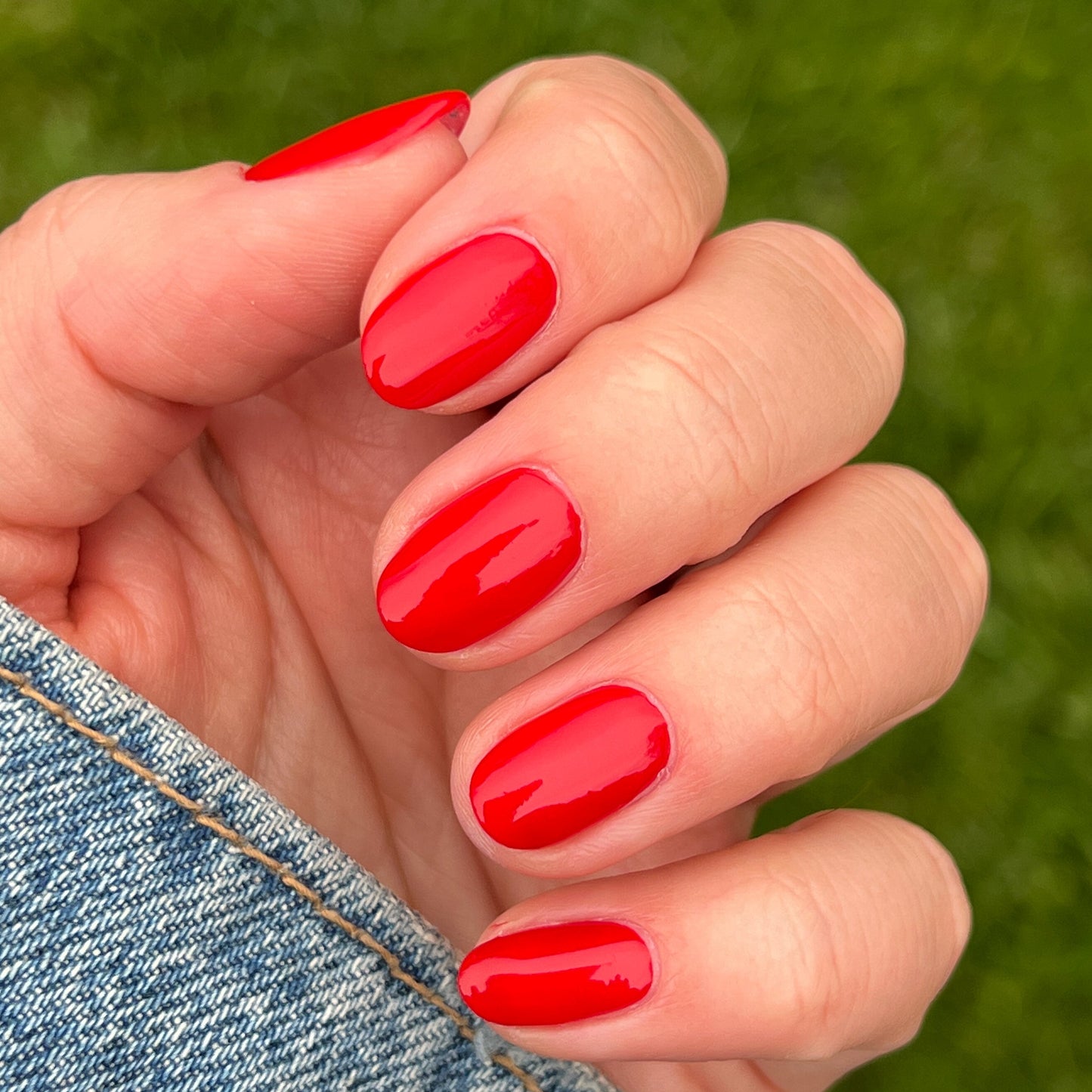 Fingernails painted with glossy Lollipop quick dry polish in bright cherry red against outdoor grass background
