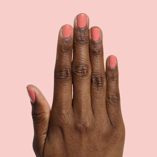 Hand with neatly trimmed nails painted bright coral orange in Carrot Juice gel polish by Olive and June