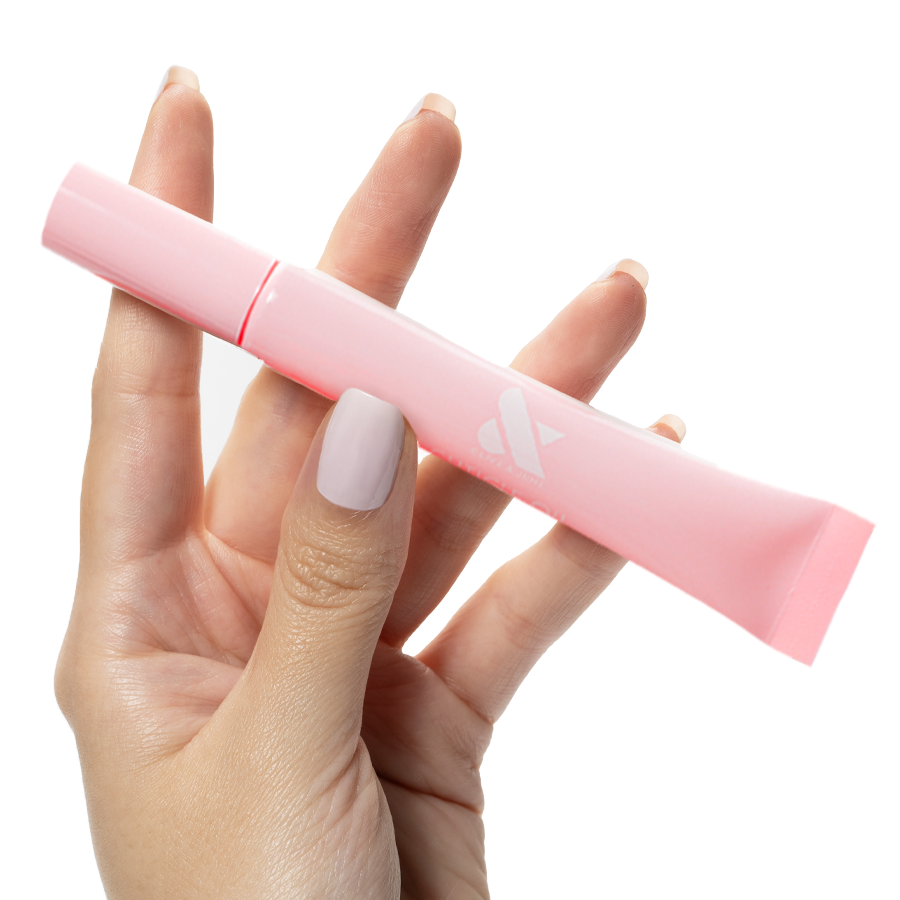 Hand holding a slim pink tube of Cuticle Oil designed to nourish and hydrate cuticles for healthy mani care.