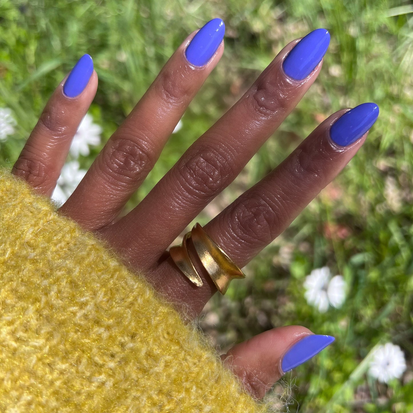 Hand with Royal quick dry gel polish in vibrant blue-purple on natural nails outdoors with green grass and white flowers background