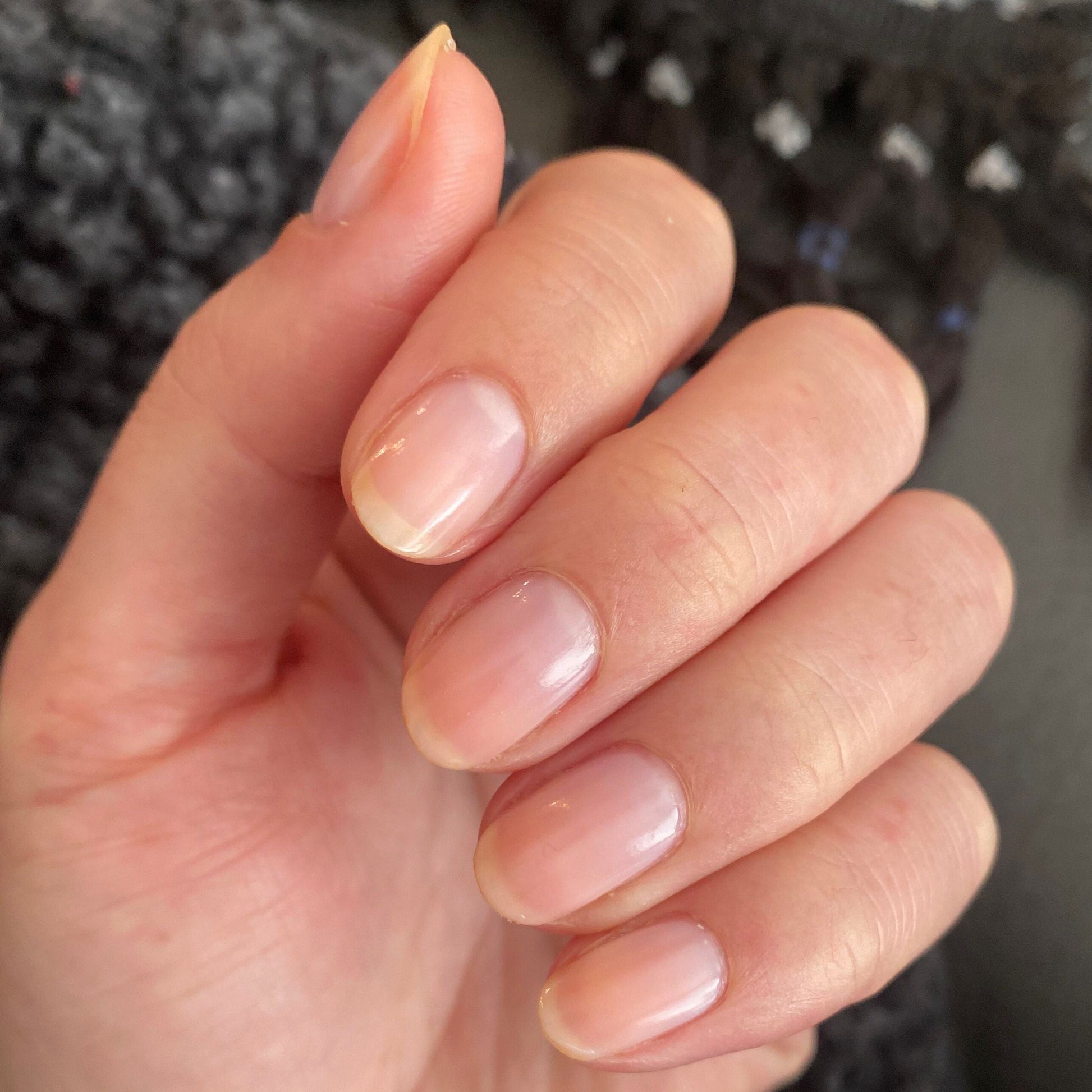 Hand with nails coated in CCT sheer neutral pastel pink polish for a soft and natural manicure finish