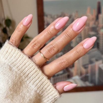 Hand with almond-shaped nails painted in milky sheer pink Dream Job - Gel polish against blurred cityscape background