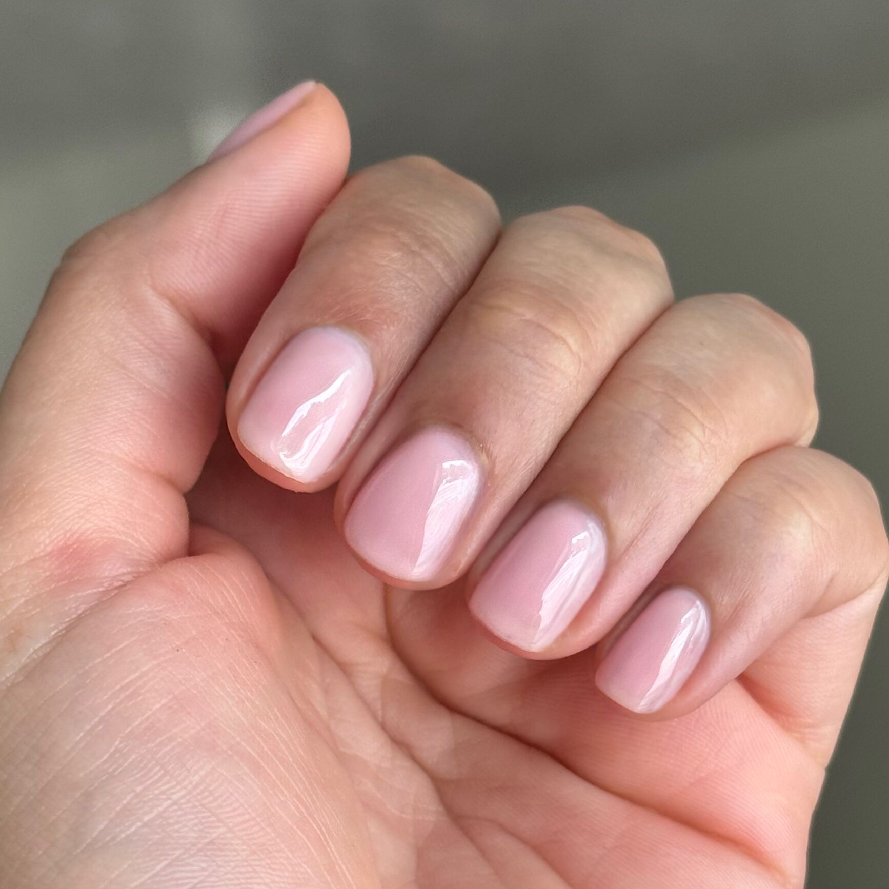 Close-up of hand with short nails polished in milky sheer pink Dream Job - Gel for a natural manicure look