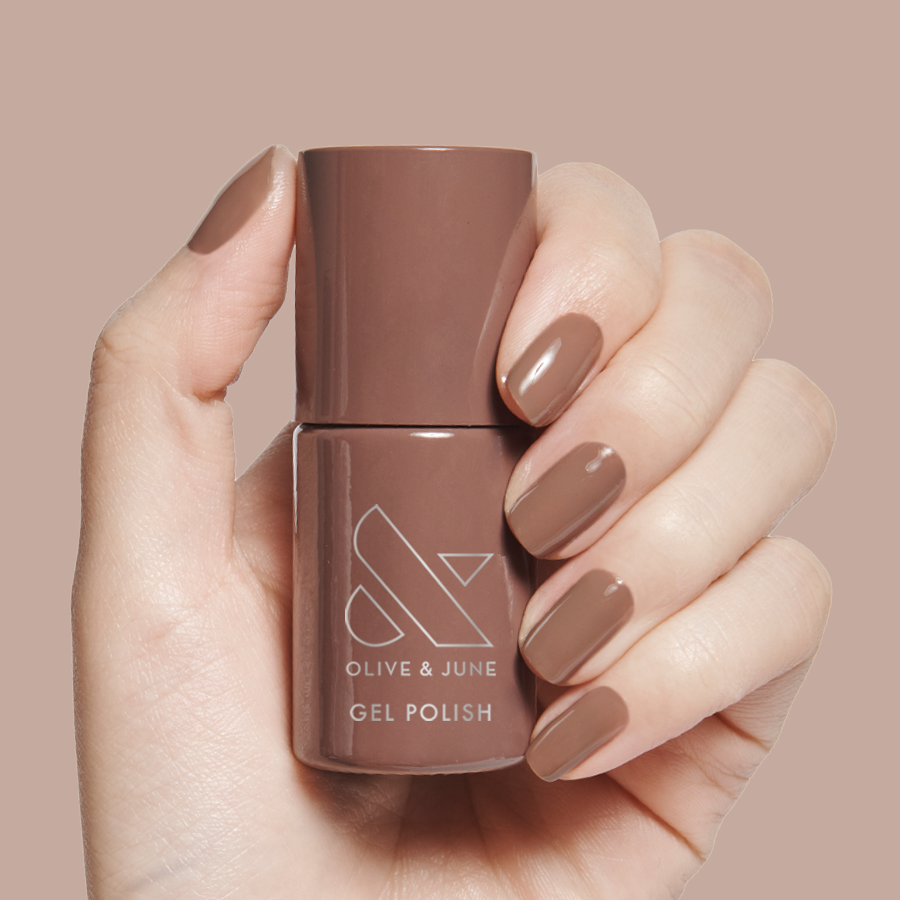 Hand holding Fawn - Gel polish bottle with matching brown neutral gel mani on a beige background