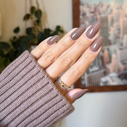 Hand with glossy Fawn - Gel polish in soft minky brown neutral shade, manicured nails with gold ring and cozy sweater sleeve