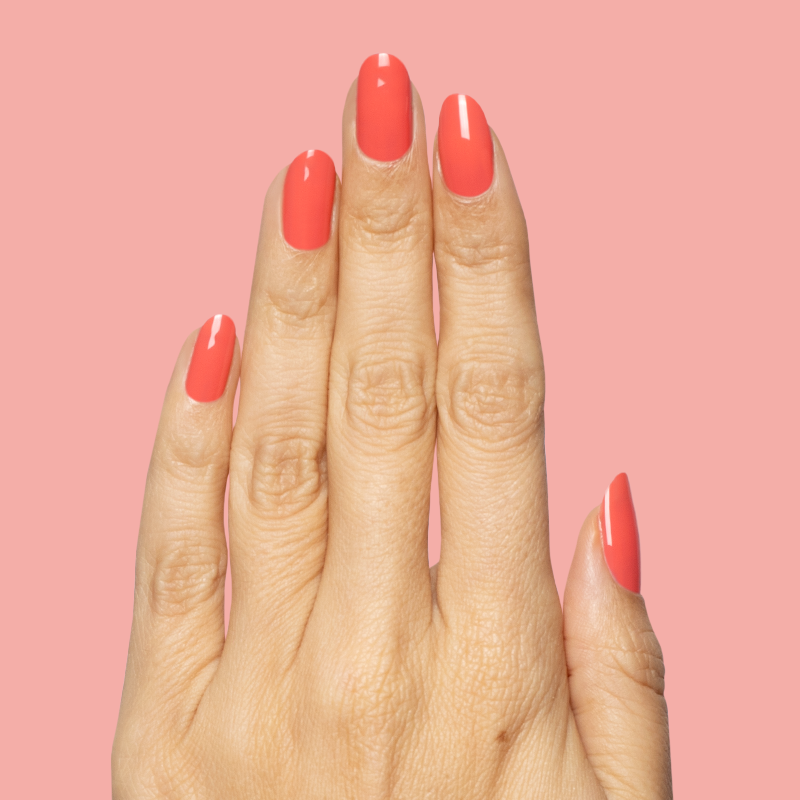 Hand with smooth nails polished in bright watermelon red using Field Day - Gel on soft pink background