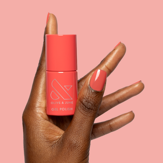 Hand holding Field Day - Gel polish bottle with nails painted in juicy watermelon red on soft pink background