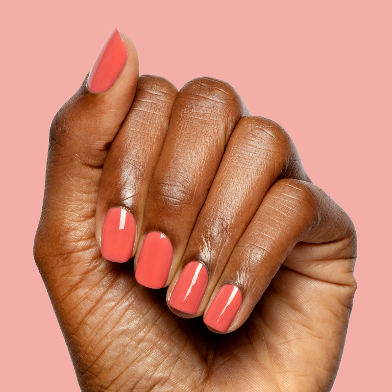 Close-up of hand with nails painted in glossy coral pink using Field Day - Gel polish on light pink background
