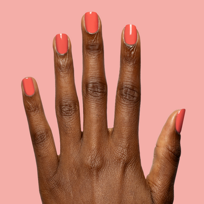 Hand with nails painted in glossy bright coral red using Field Day - Gel against soft pink background