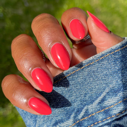 Hand with almond-shaped nails painted in Field Day bright watermelon red long-lasting polish against denim fabric background