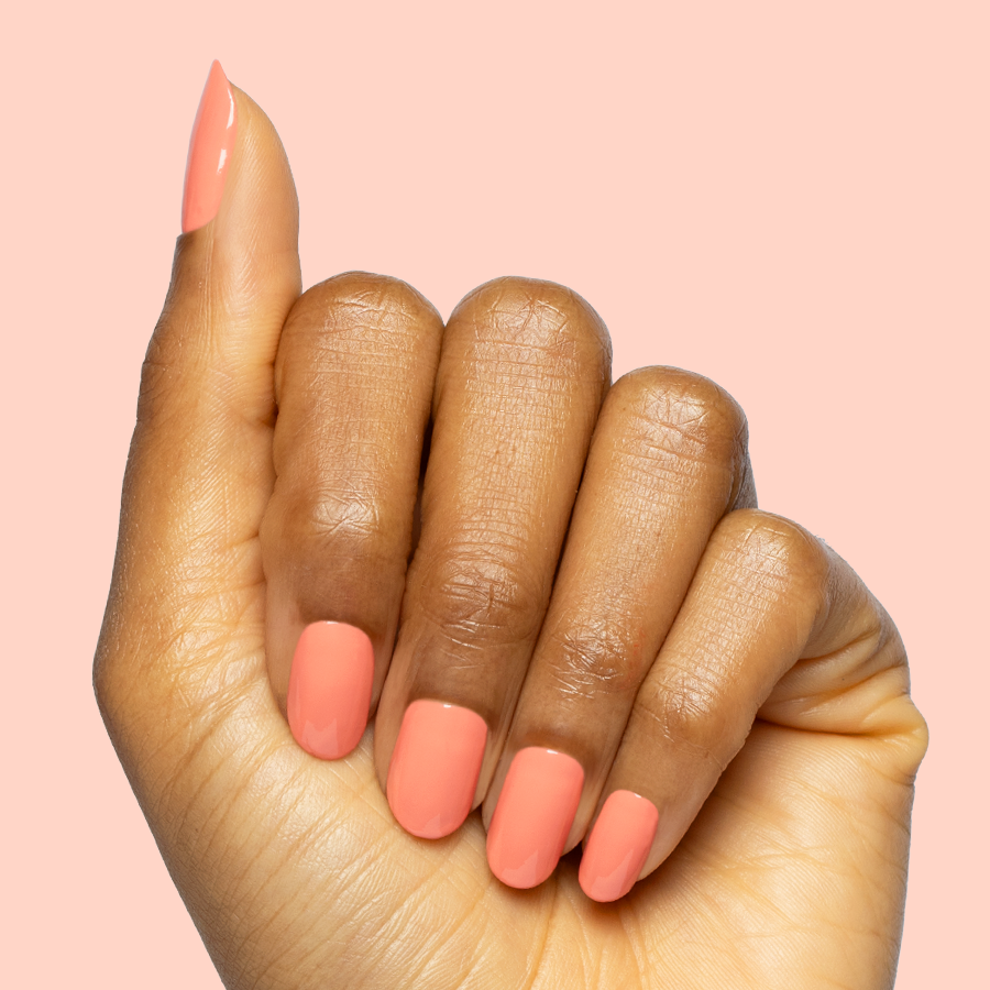 Hand with square-shaped nails painted in bright orangey coral Frolic quick dry gel polish on pale pink background