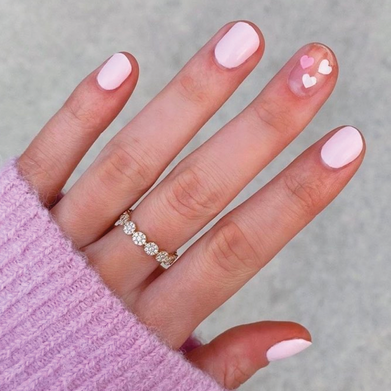 Hand with nails painted in GH, a soft opaque baby pink polish with heart accents for a charming at-home manicure
