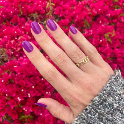 Hand with nails painted bright neon purple Grape Soda polish showing smooth glossy manicure with vibrant floral background