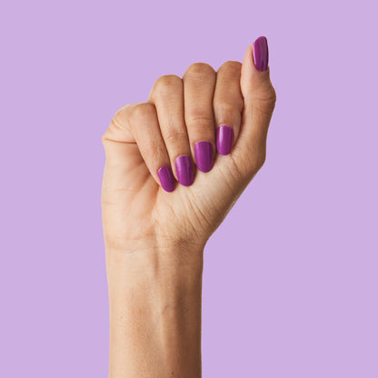Hand with nails painted vibrant purple polish from Grape Soda showing glossy at-home mani on lavender background