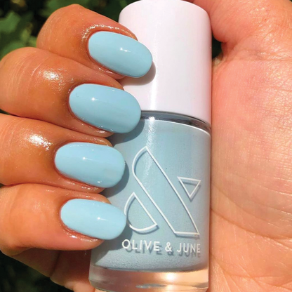 Hand with nails painted in Honest & True soft blue polish holding Olive & June bottle for a smooth at-home manicure