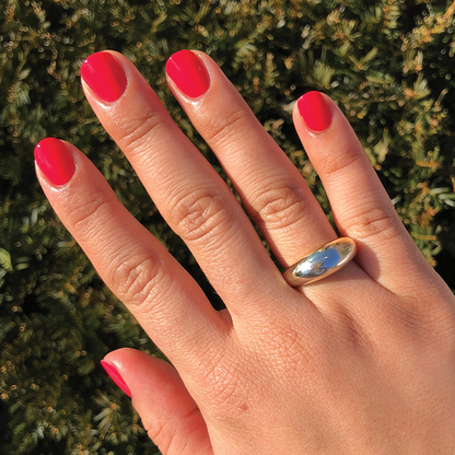 Hand with a smooth, glossy Hibiscus polish manicure in bright tropical pink wearing a simple silver ring outdoors