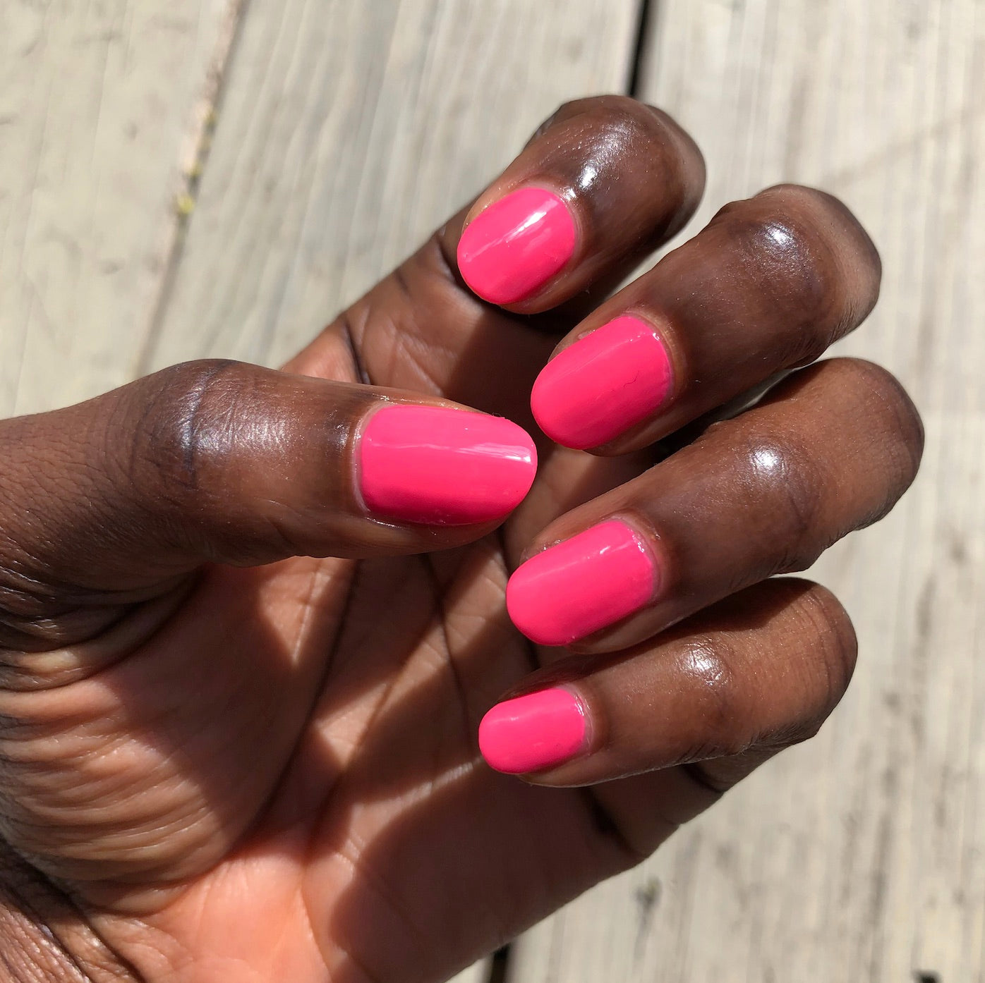 Hand with nails painted in bright Hot Strawberry gel polish showing glossy, vivid pink for at-home manicure or quick dry polish.