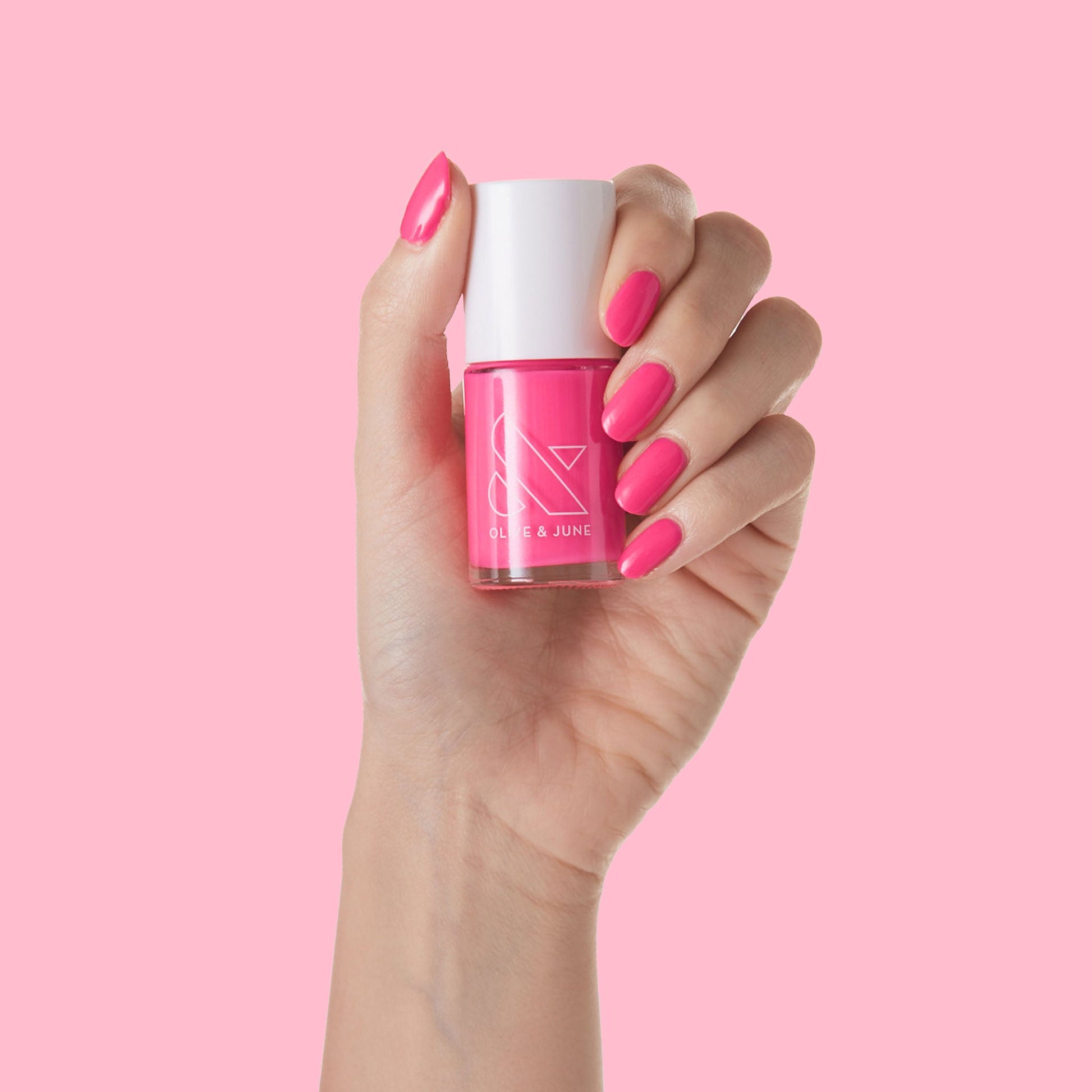 Close-up of a hand holding Hot Strawberry polish with nails painted in bright, nearly neon pink for at-home mani.