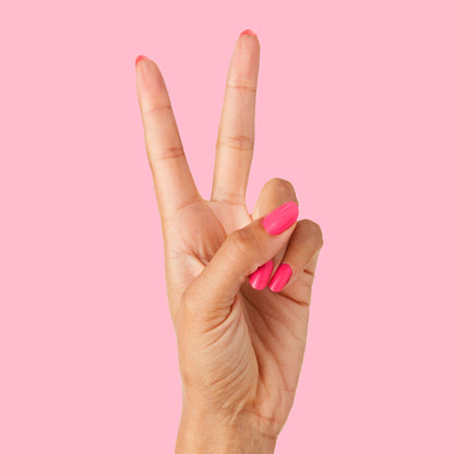 Hand showing two fingers with bright neon pink Hot Strawberry long-lasting gel polish on nails against pink background