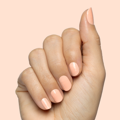 Hand with smooth nails painted in soft pastel melon shade It’s Serving Melon Cocktails for a fresh at-home manicure