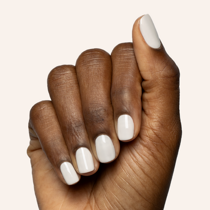 Hand with short rounded nails polished in soft off-white shade using LHG - Gel polish on plain light background