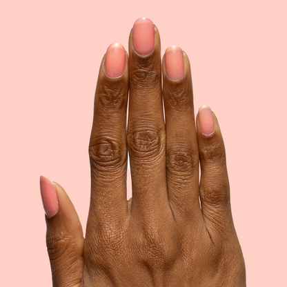 Hand with medium natural nails painted in sheer coral pink using Papaya Gloss polish on soft peach background