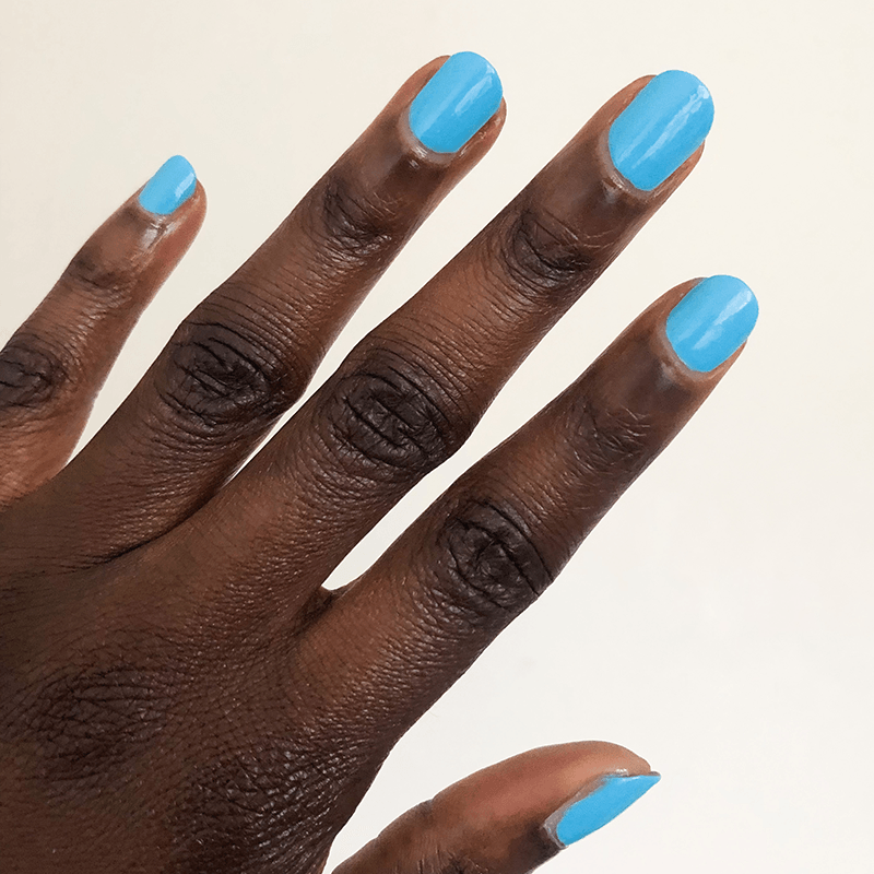 Hand with nails painted in bright Megababe Blue gel polish showing a fresh, confident at-home manicure look