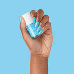 Hand with nails painted in bright Megababe Blue gel polish holding matching blue Olive and June bottle against blue background
