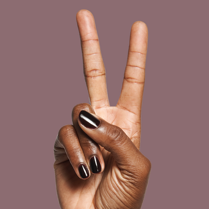 Hand with dark skin tone showing nails painted in Covet - Gel polish, a cool deep plum shade on a muted mauve background
