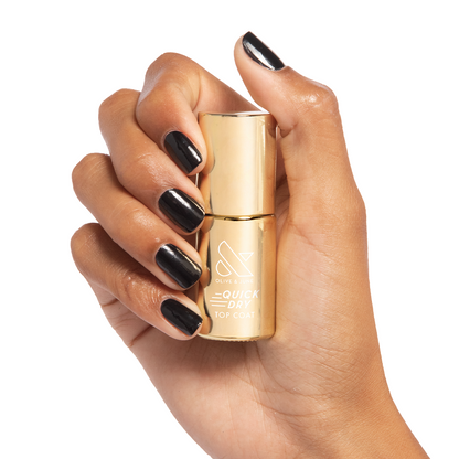 Hand holding Olive and June Quick Dry Top Coat bottle with glossy black polished nails in bright light