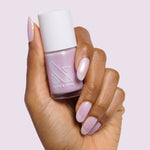 Hand with almond-shaped nails painted in glossy Purple Puka gel polish holding bottle of milky lavender iridescent polish