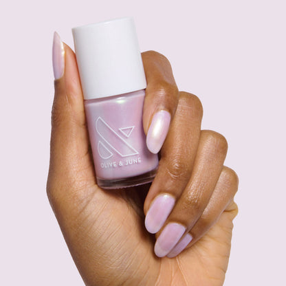 Hand with almond-shaped nails painted in glossy Purple Puka gel polish holding bottle of milky lavender iridescent polish