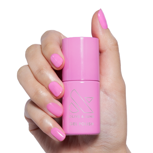 Permanent Vacation - Gel bright pink gel polish bottle held by hand with matching polished nails for mani or pedicure
